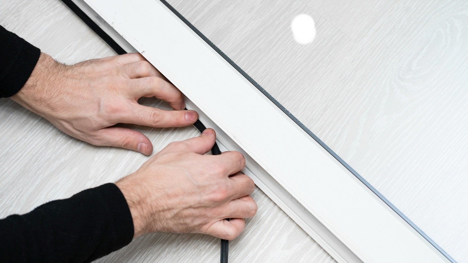 Two hands pressing weatherstripping into the gap around a white door to seal it.
