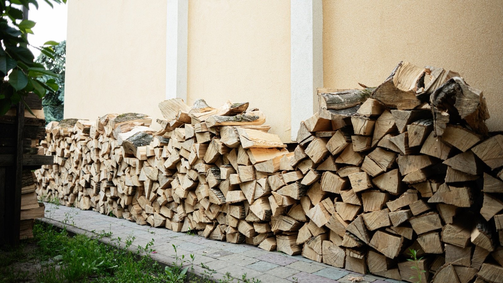 A long stack of split firewood piled directly against the exterior wall of a house.